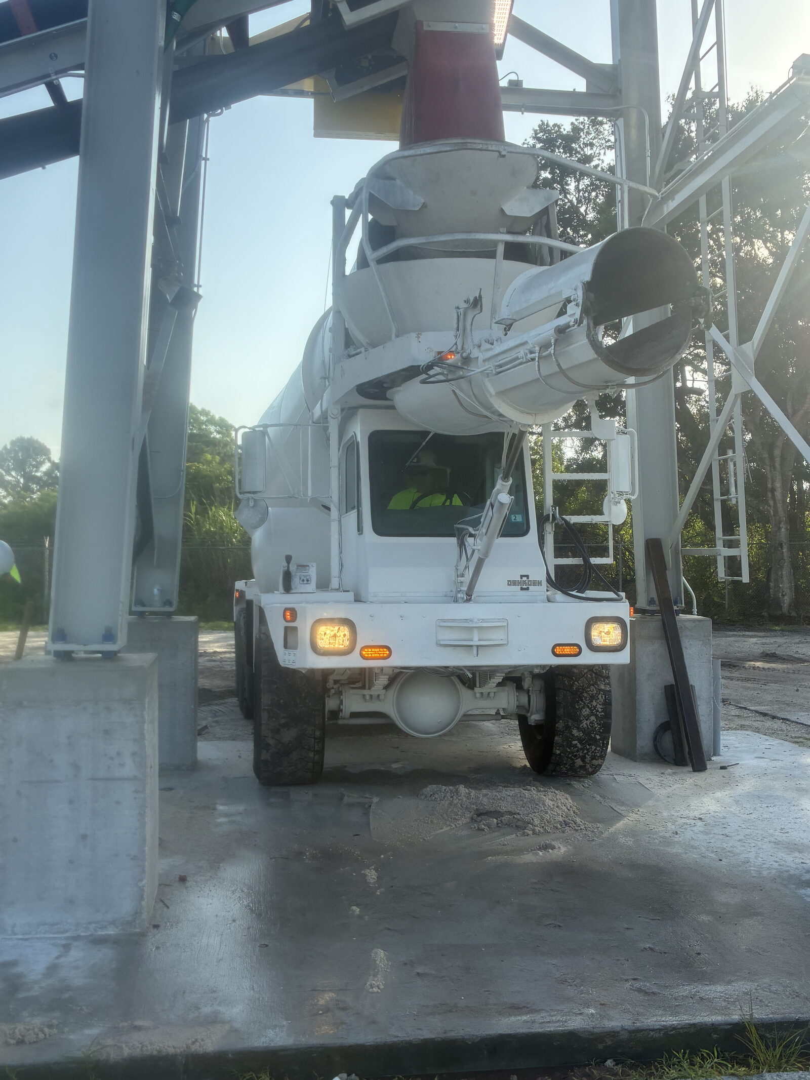 Rear view of a TEC mixer truck loading under the plant hopper, the driver visible in the cab in hi-vis.