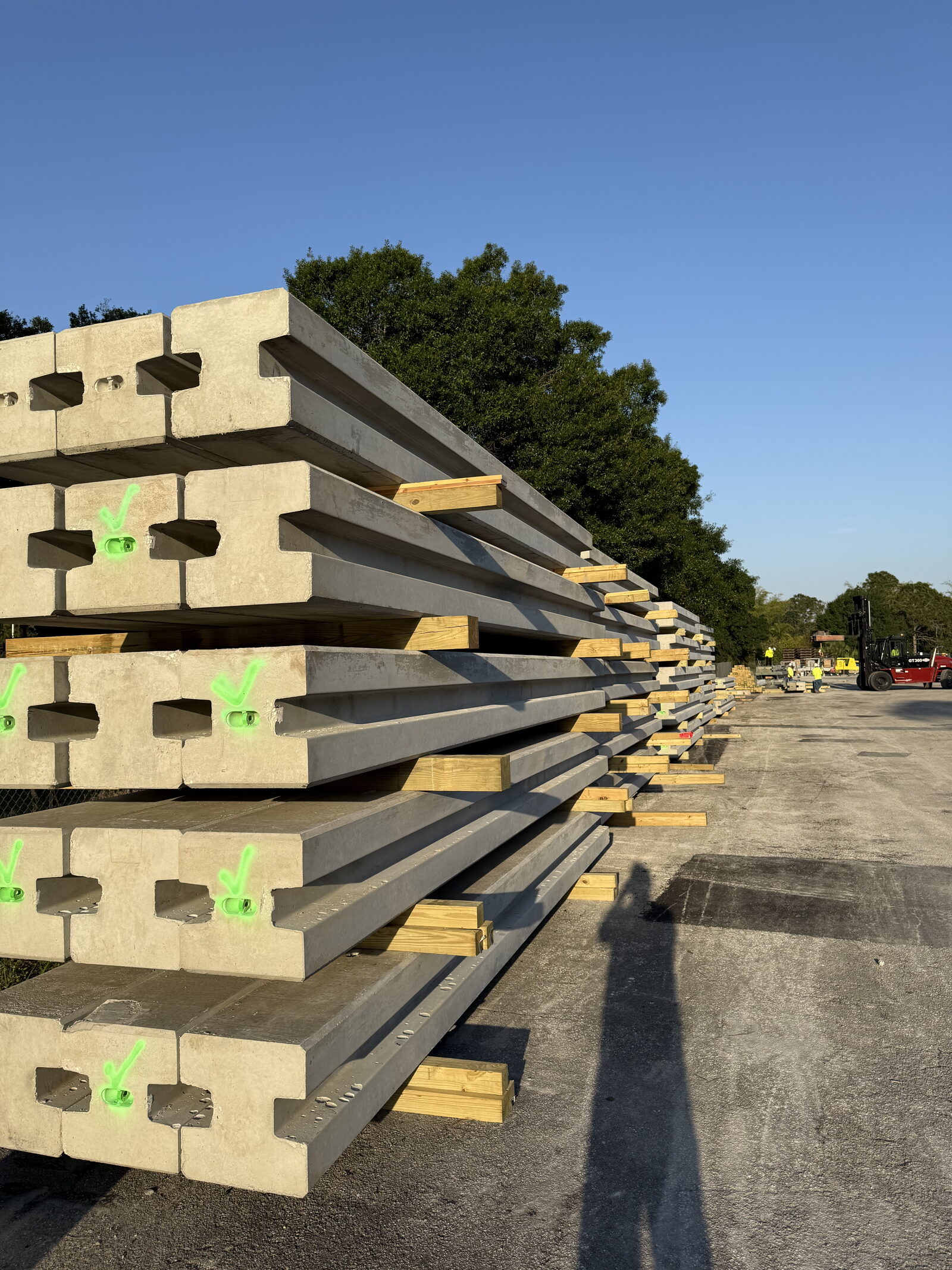 Rows of freshly cast precast wall panels and posts stacked on dunnage in the Triple E yard, a forklift working at the far end.