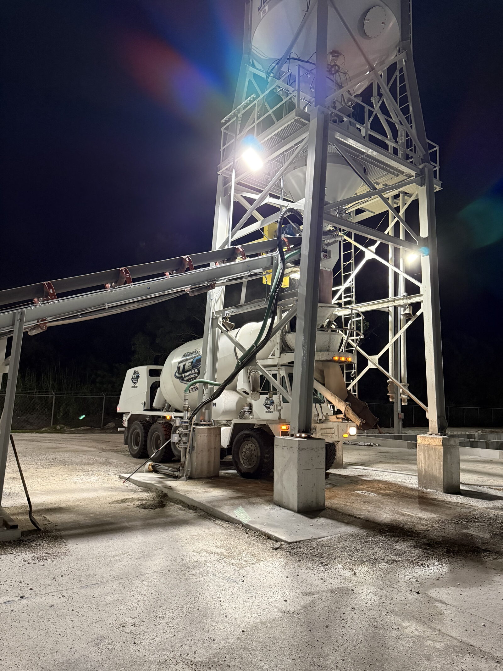 The Indiantown batch plant at night — the silo tower and floodlights over a TEC mixer truck, fresh concrete pad in the foreground.