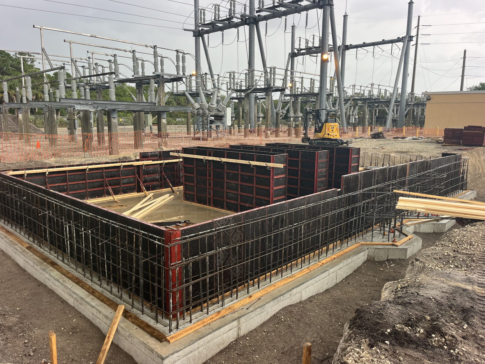 Red-framed wall forms rising from the footing at a substation site, a mini excavator working behind.