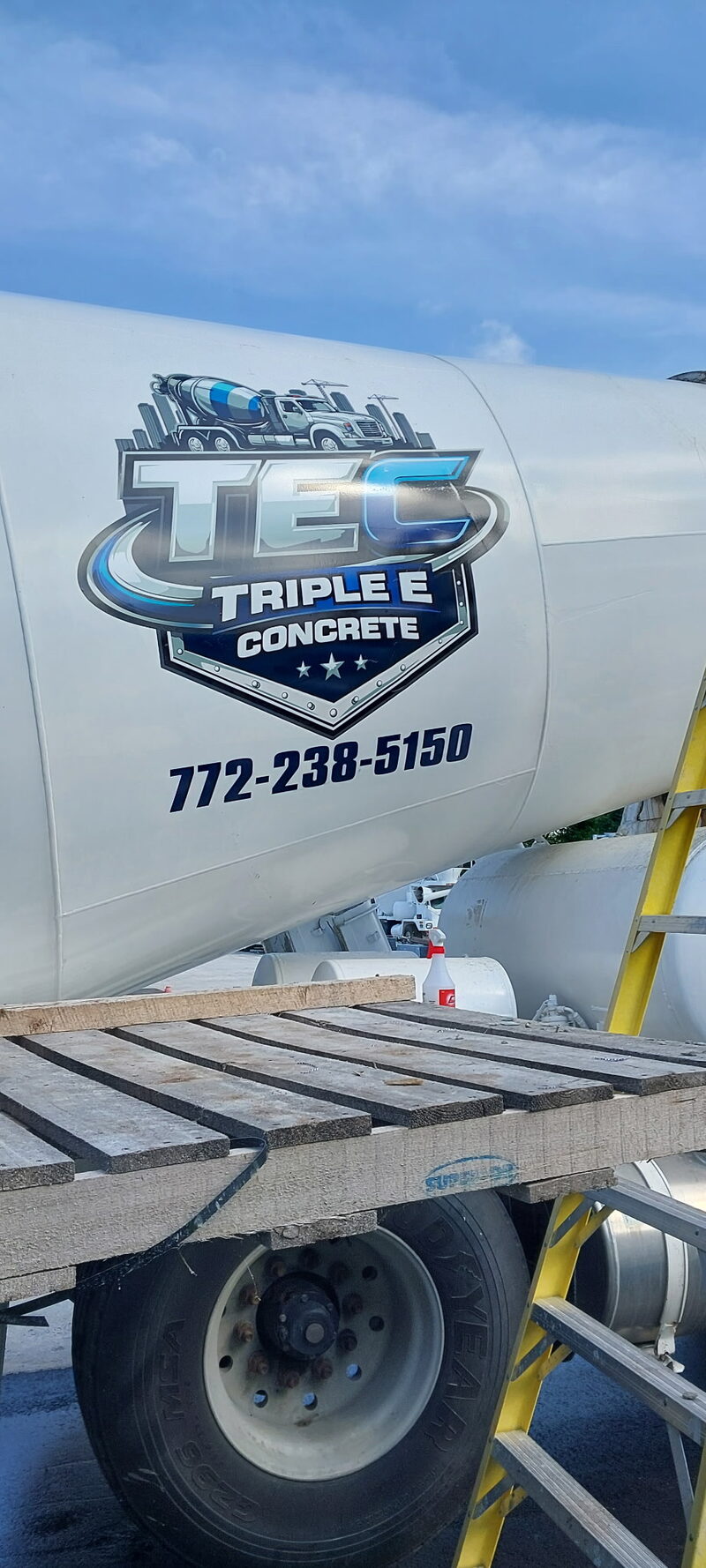 The TEC shield decal and phone number painted on a mixer drum against blue sky.